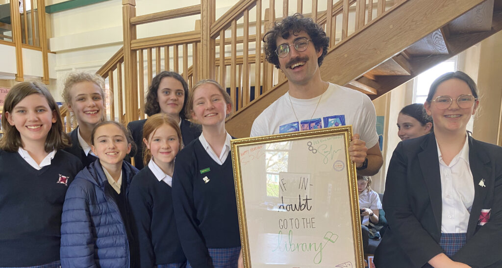 students and teacher holding a handmade sign for a library