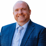 A head and shoulders image of the Acting Head of Exeter School for 2025-2026 academic year is a smiling man in a blue suit with flowery tie