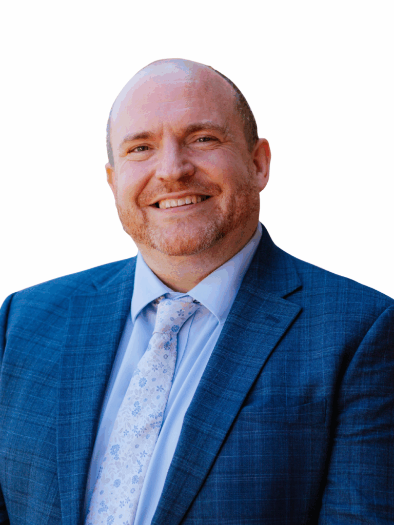 A head and shoulders image of the Acting Head of Exeter School for 2025-2026 academic year is a smiling man in a blue suit with flowery tie