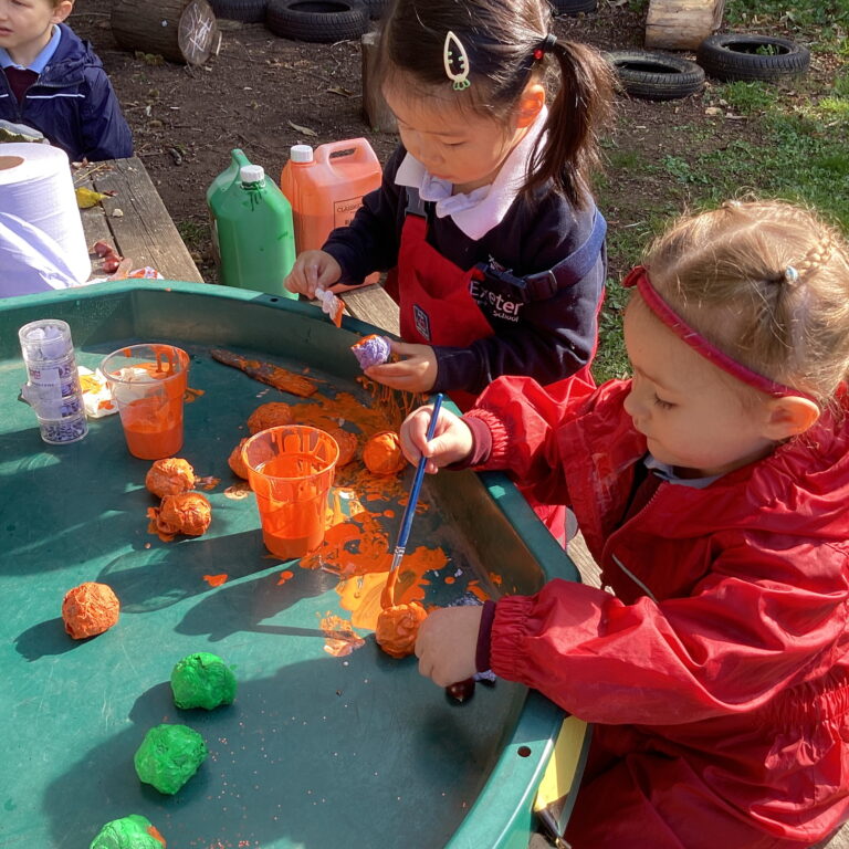 Children painting orange and green balls at outdoor tray table
