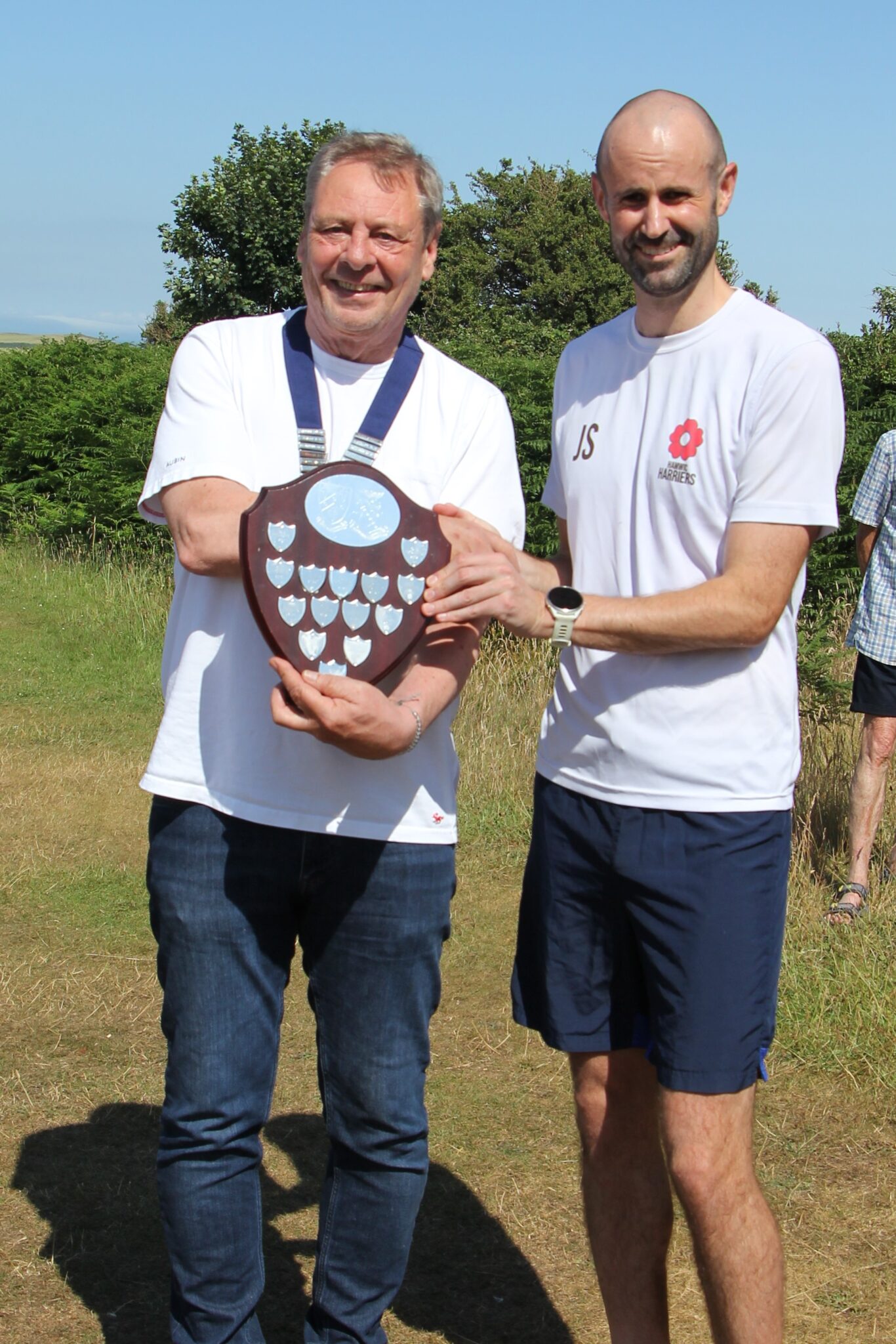 Two men holding an award shield trophy in a field