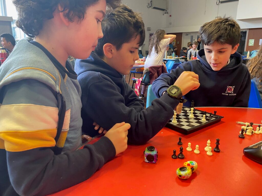 3 young boys playing and observing chess at a red table