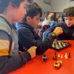 3 young boys playing and observing chess at a red table