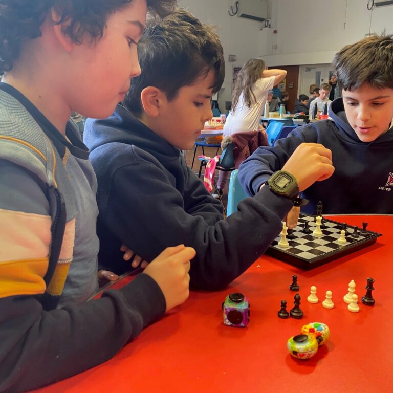 3 young boys playing and observing chess at a red table