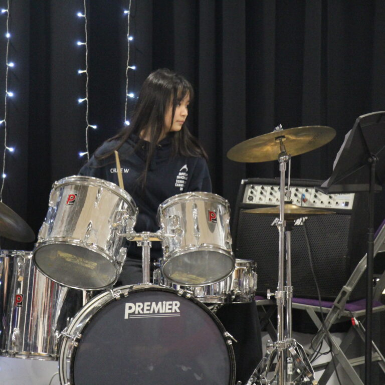 A pupil playing a Premier drum kit on a darkened stage with fairy lights in the background.