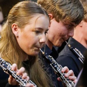 Close up photo of mix of boys and girls in their teens playing the oboe in an orchestra