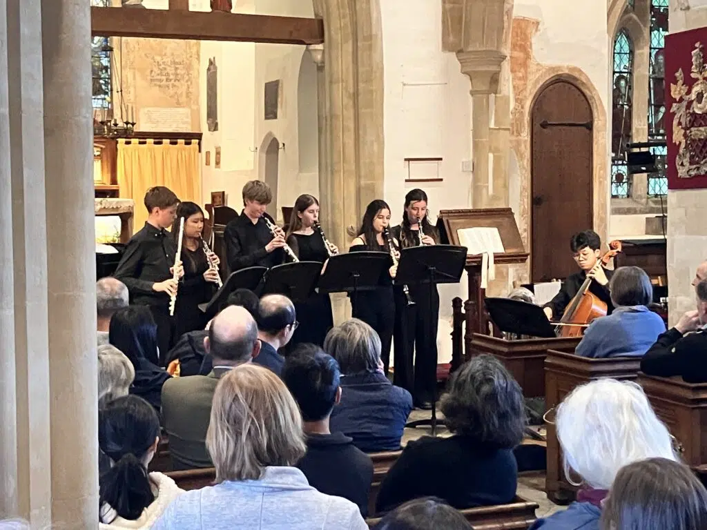 Young musicians playing wind instruments in a church, facing music stands as the audience watches a concert.