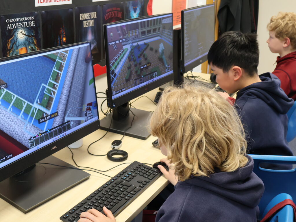 Three children seated at computers playing Minecraft in a classroom.