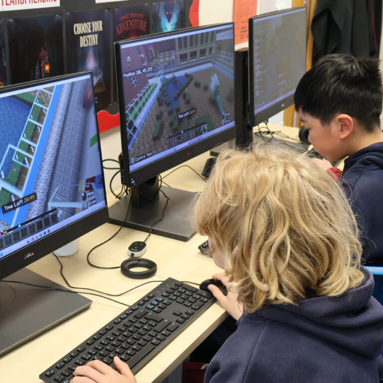 Three children seated at computers playing Minecraft in a classroom.