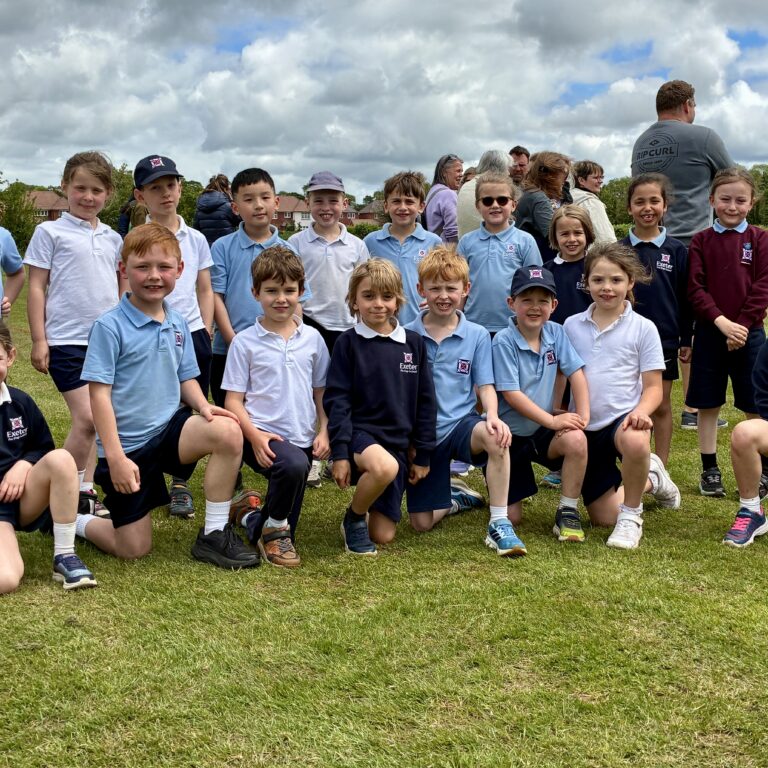 Group of children in blue and navy school uniforms posing on a grassy field outdoors.