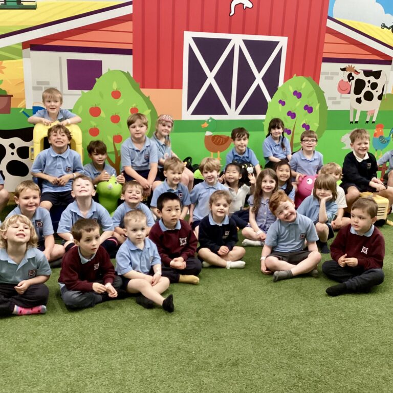 Group of smiling preschoolers in blue uniforms posing on a green floor with a bright farm mural backdrop.