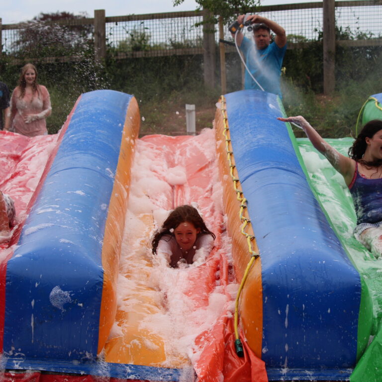 People enjoy a colorful inflatable water slide ride outdoors with foam splashing around.