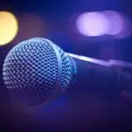 Close-up of a wired microphone on stage with blue and purple lighting in the background, ready for a performance or speech.
