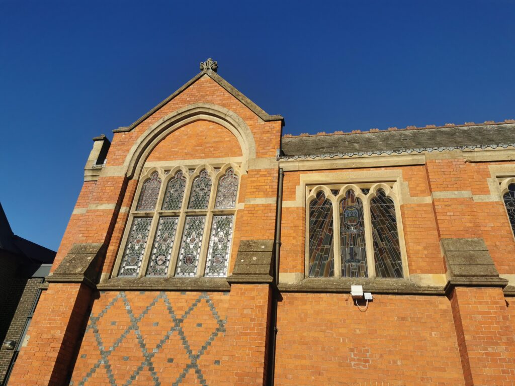 Brick church facade with tall arched, stained-glass windows and stone trim set against a clear blue sky.