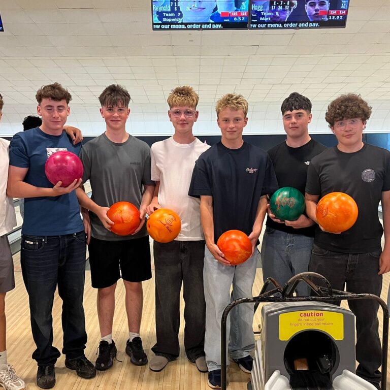 A group of ten young men standing side by side in a bowling alley, each holding a colored bowling ball and posing for the photo.