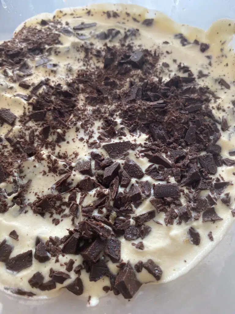 Close-up of light-colored batter in a bowl topped with lots of dark chocolate shavings.