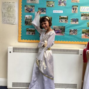 Girl in a silver costume with a gold belt posing in front of a teal school display board with photos and the words 'Problem Solving' and 'Resilience'.