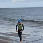 Boy running out of the sea with sim cap and wet suit on.