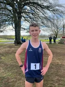 Young male runner wearing a blue and maroon Exeter School singlet with bib number 1, posing outdoors after a race.