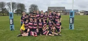 Youth rugby team of players in maroon and navy striped jerseys posing together on a grass field with padded goalposts in the background.