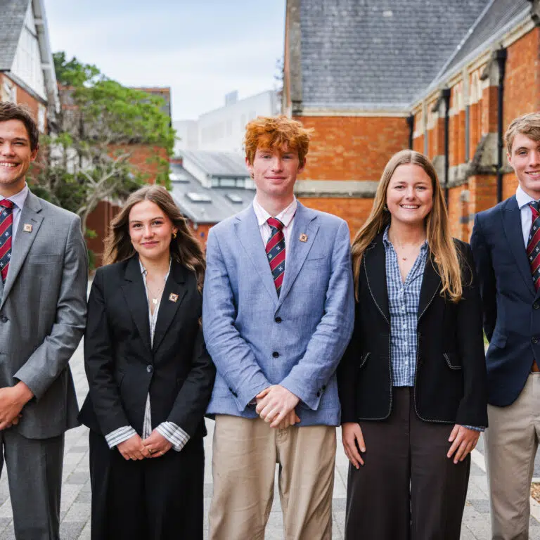 Five senior sixth form pupils in business dress standing in quad with red brick buildings around