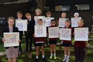 Group of schoolchildren outdoors, each holding framed colorful heart artwork for a class project.