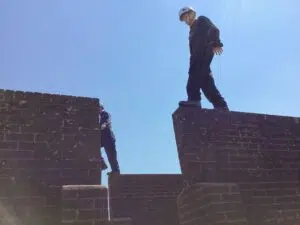 Construction worker with a white hard hat standing on a brick wall against a clear blue sky.