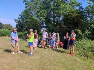 Group of people standing in a sunny park, chatting with trees behind them.