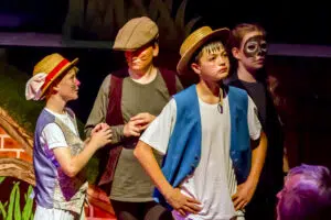 Group of children in animal-themed costumes and face paint on a stage, wearing hats and colorful outfits.