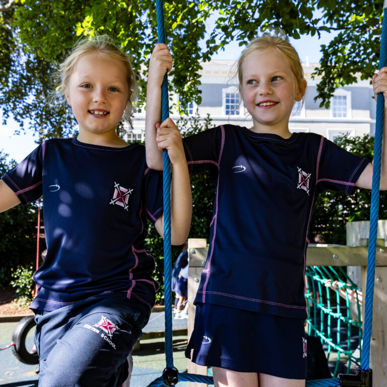 Two young girls in navy school uniforms climb a rope obstacle on an outdoor playground.