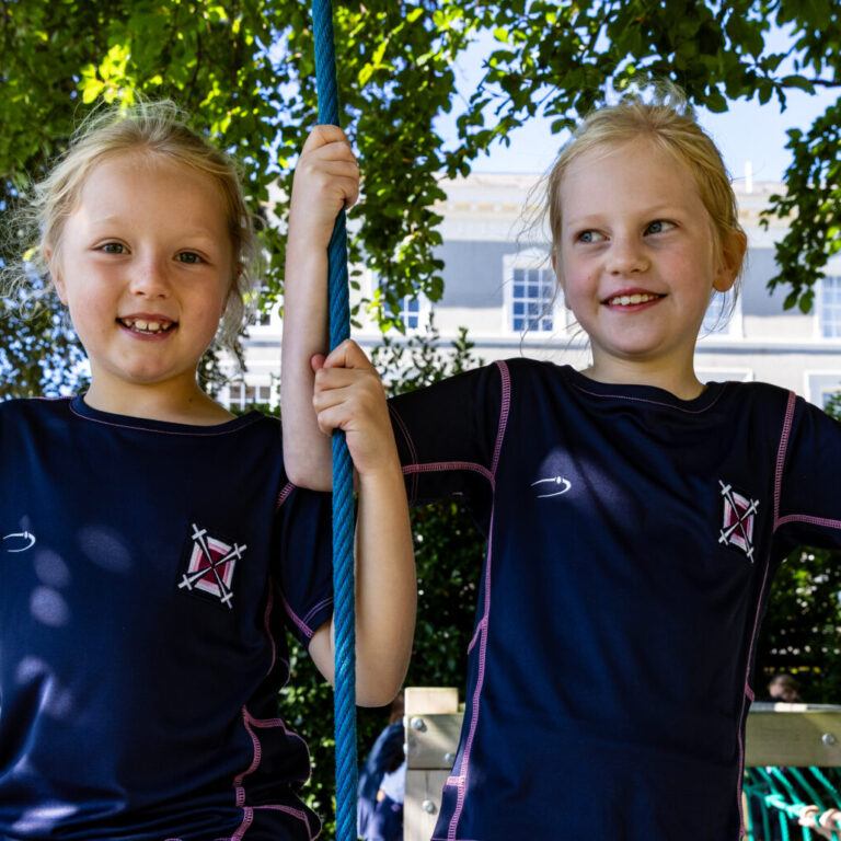 Two young girls in navy school uniforms climb a rope obstacle on an outdoor playground.