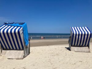 Two blue-and-white striped beach chairs sit in the sand, facing the calm ocean under a clear sky.