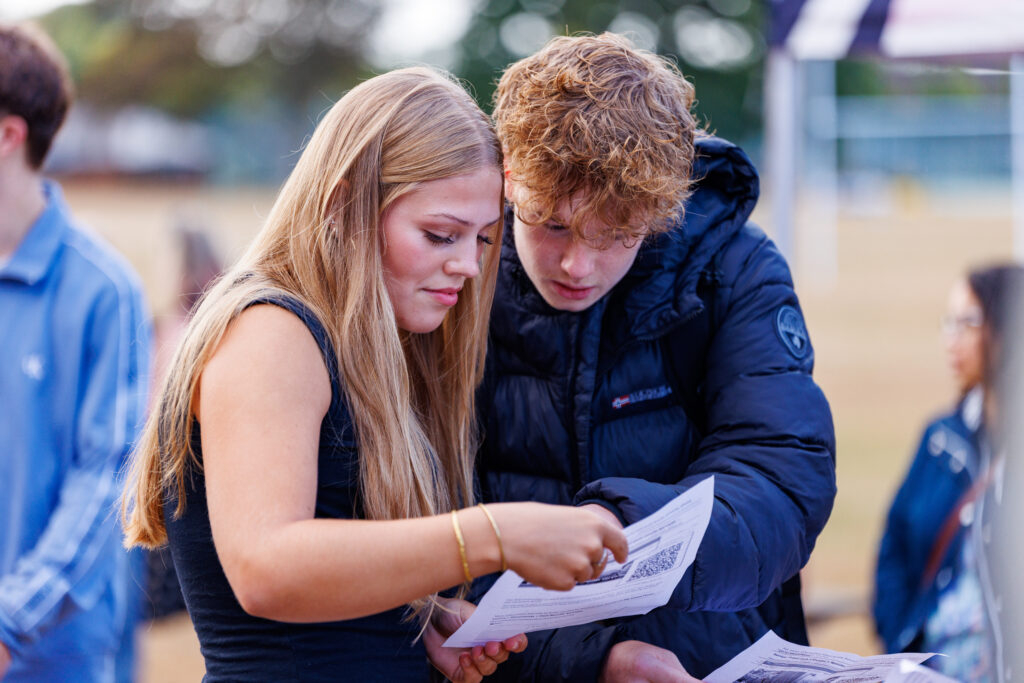 Two young adults outdoors, closely reading documents together.