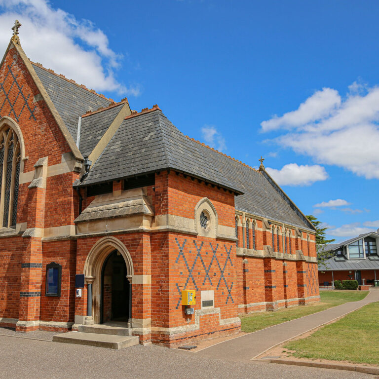 Red-brick church with a Gothic arched window, stone detailing, and a slate roof against a bright blue sky