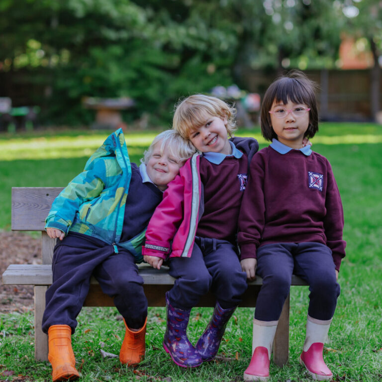 3 children sitting on a bench in welly boots and coats