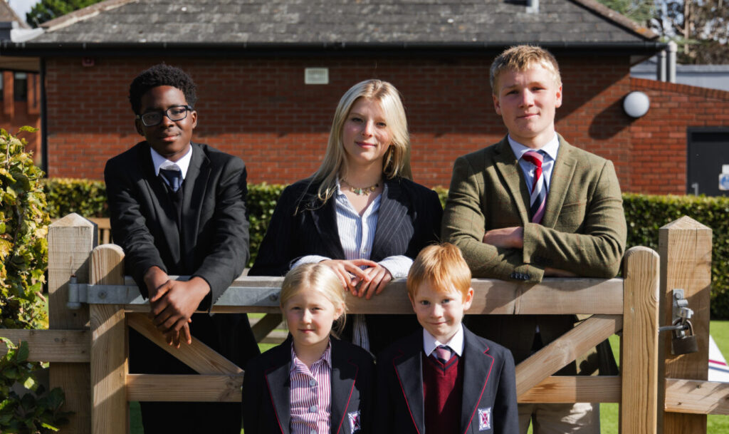 A group of five pupils from junior school, senior and sixth form showing diversity over a fence gate with greenery around