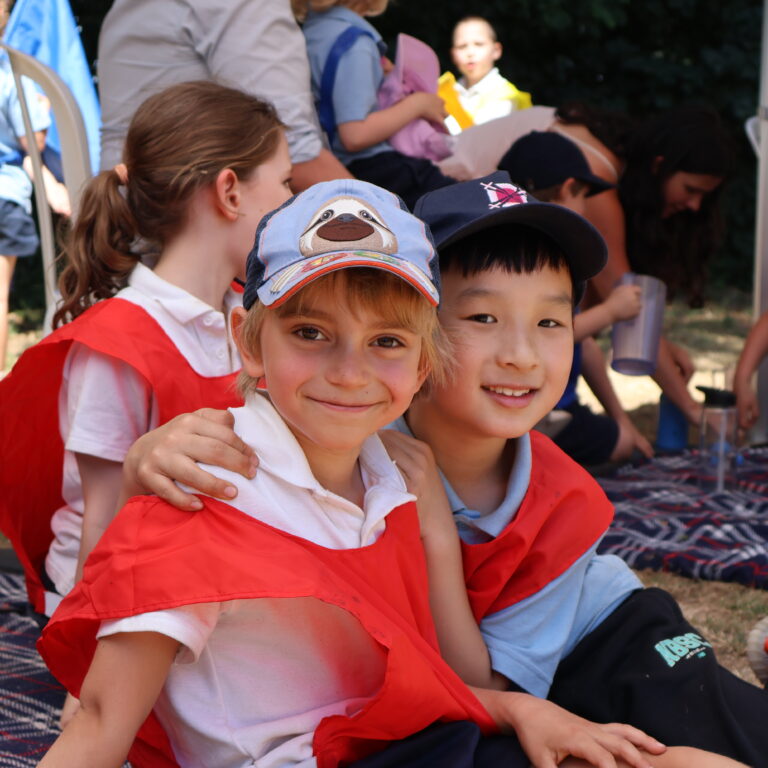 two boys in red bibs smiling and sat down in the floor with young people behind them