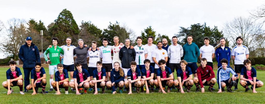 Team of young football players in school kit posed in front of older players in their own mixed kits who have come back to their old school to play a game for memories.