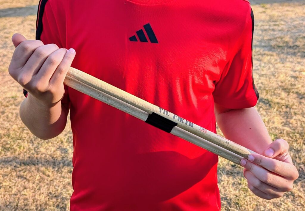 Someone holding drumsticks with a red tshirt on