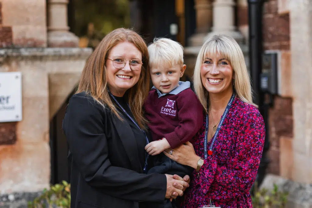 EXESCHOOL 16 Copy – Exeter School 2 ladies standing outside the school holding a small boy smiling at the camera